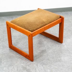 May include: A mid-century modern footstool with a rectangular, padded seat in a muted olive green. The frame is constructed of warm-toned wood, featuring a simple, open design. The stool is approximately 18 inches long, 12 inches wide, and 16 inches high.