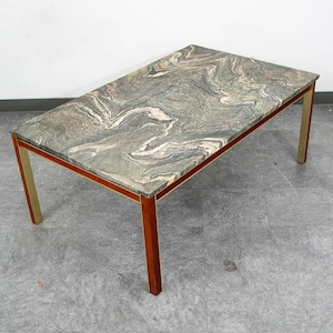 May include: A rectangular coffee table featuring a polished stone top with a swirling pattern of gray, green, and cream veins. The table is supported by four straight legs constructed from dark wood with vertical metallic gold-toned accents.