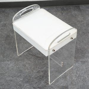 May include: A rectangular white tray table featuring clear acrylic side panels that extend upward to form integrated handles. The white surface is framed by the transparent acrylic structure, which is secured with visible metal hardware on the sides.