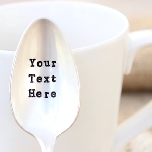 May include: A silver teaspoon with the text "Your Text Here" engraved on the front. The spoon is sitting in a white coffee mug.