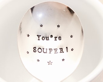 Puede incluir: Un cucharón de sopa de plata con las palabras "You're Souper!" grabadas en la parte delantera. El cucharón está rodeado de pequeñas estrellas.
