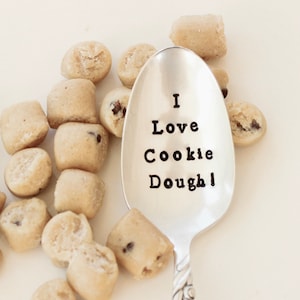 May include: A silver spoon with the words "I Love Cookie Dough!" engraved on it. The spoon is surrounded by small balls of cookie dough.