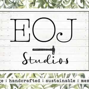 K&ouml;nnte beinhalten: Ein wei&szlig;es Holzschild mit schwarzem Text, der "EOJ Studios" lautet, mit einer kleinen schwarzen Hammergrafik unter dem Text. Der Text "vintage : handcrafted : sustainable : memories" ist unter dem Schild gedruckt.
