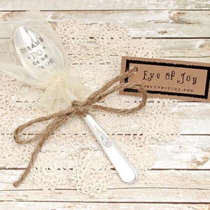 May include: A silver spoon with the words "Dreams Do Come True" engraved on it. The spoon is wrapped in a white tulle bag and tied with twine. A brown tag with the text "Eye of Joy" and a website address is attached to the twine.