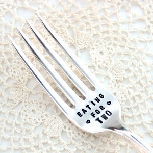 May include: A silver fork with the words "Eating for Two" engraved on the handle. The fork is on a white crocheted surface.