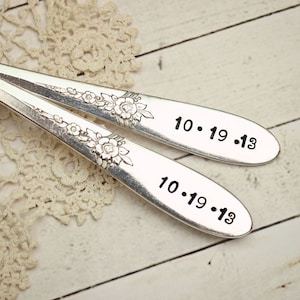 K&ouml;nnte beinhalten: Zwei silberne L&ouml;ffel mit floralen Designs, die mit dem Datum 10.19.13 graviert sind.