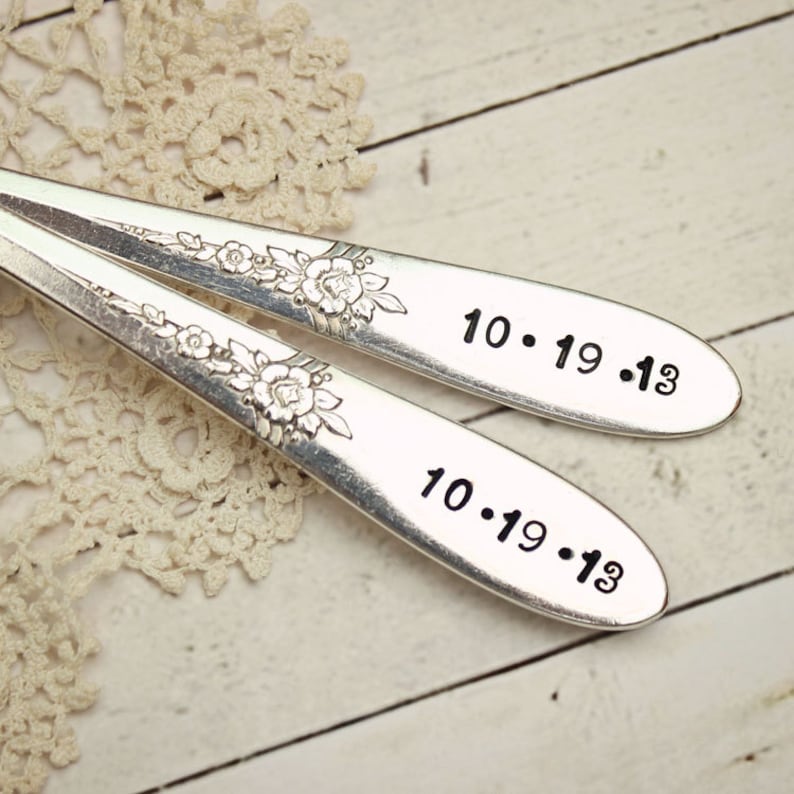 K&ouml;nnte beinhalten: Zwei silberne L&ouml;ffel mit floralen Designs, die mit dem Datum 10.19.13 graviert sind.