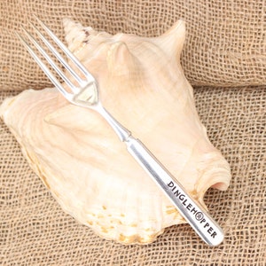 May include: Silver fork with a seashell design on the handle. The fork is engraved with the words "Dinglehopper".