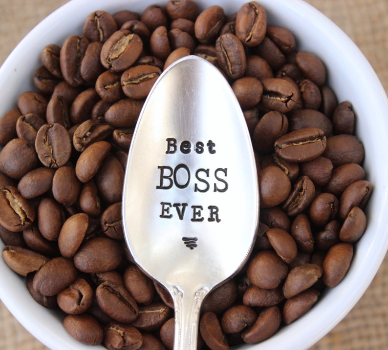 May include: A silver spoon with the words "Best Boss Ever" engraved on it, surrounded by coffee beans.