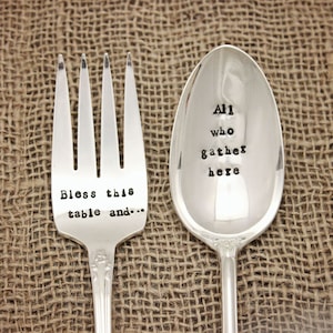 May include: A set of two silver utensils with engraved sayings. The fork says "Bless this table and..." and the spoon says "All who gather here".