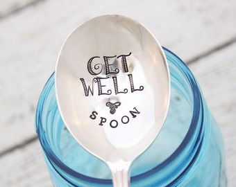 Puede incluir: Una cuchara de plata con las palabras "Get Well Spoon" grabadas. La cuchara está en un frasco de vidrio azul.