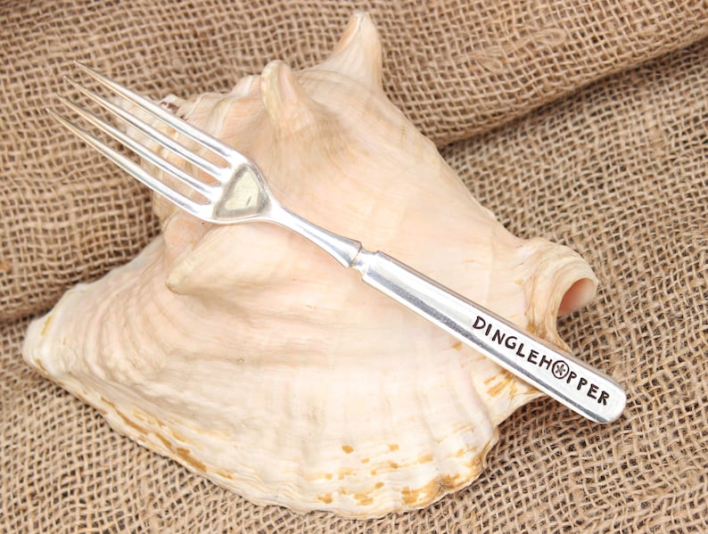 May include: Silver fork with a DINGLEHOPPER logo engraved on the handle, resting on a seashell.
