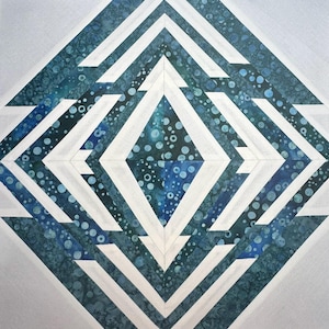 May include: A square quilt block featuring a geometric diamond pattern. The design consists of alternating strips of solid white fabric and a dark teal blue fabric with a mottled, bubble-like texture, arranged in concentric diamond shapes.