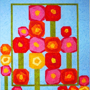 Pode incluir: Um cobertor com fundo azul e moldura verde. Dentro da moldura, há cinco fileiras de flores geométricas coloridas em tons de vermelho, laranja, rosa e amarelo. As flores são dispostas em um padrão simétrico.