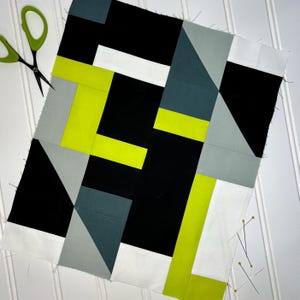 Könnte beinhalten: Geometrischer Patchwork-Quilt in Schwarz, Weiß, Grau und Neongrün. Der Quilt hat ein modernes abstraktes Design mit verschiedenen Formen und Winkeln. Eine grüne Schere und Stecknadeln sind sichtbar.