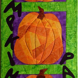 May include: A quilted wall hanging featuring three orange pumpkins with brown stems against purple and green backgrounds. The words "My Pumpkin Patch" are stitched in black along the side. A festive, handmade autumn decoration.