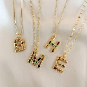 May include: Four gold necklaces with colorful jeweled letter pendants. The letters spell out "BME" in a gold chain necklace with colorful jeweled letters.