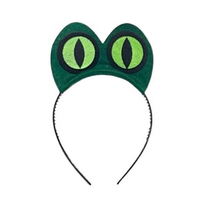 May include: Green felt headband with two large green eyes. The headband is black and has a simple design.