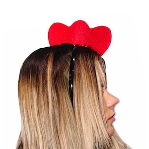 May include: A black headband with two red felt hearts attached to the top. The headband is worn on a person's head.