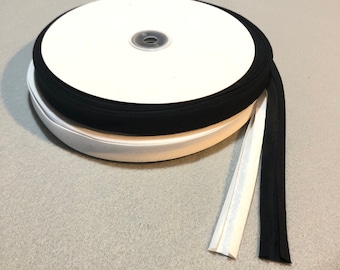 May include: A roll of black and white elastic fabric with a white backing. The elastic is folded and rolled up on a white cardboard core.