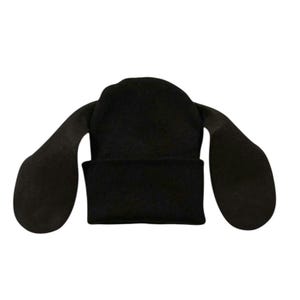May include: A solid black knit beanie featuring a cuffed brim and two long, flat, rounded fabric extensions attached to the sides, resembling floppy ears. The hat is constructed from a soft, uniform black textile material throughout.