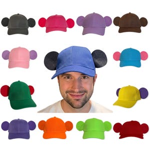 Puede incluir: Una colección de gorras de béisbol en varios colores sólidos, cada una con dos orejas redondeadas unidas a los lados. Los colores incluyen negro, rosa fuerte, morado, marrón, rosa claro, azul, turquesa, verde, amarillo, violeta, naranja, verde lima y rojo.