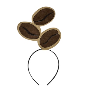 May include: A black headband with three brown coffee bean cutouts. The coffee beans have a dark brown, curved line detail. The headband is a fun accessory for coffee lovers or themed events.