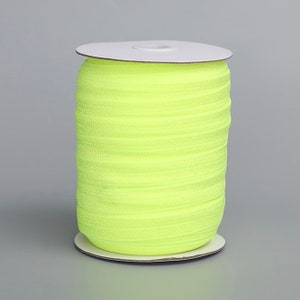 Può includere: Un rotolo di cordoncino elastico giallo brillante, avvolto attorno a un nucleo di cartone bianco.