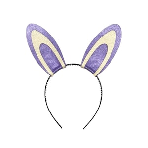 Puede incluir: Una diadema con dos orejas de conejo moradas y brillantes, con el interior de las orejas de color crema. Las orejas est&aacute;n unidas a una fina diadema de pl&aacute;stico negro. El dise&ntilde;o es sencillo y festivo, adecuado para Pascua o eventos de disfraces.