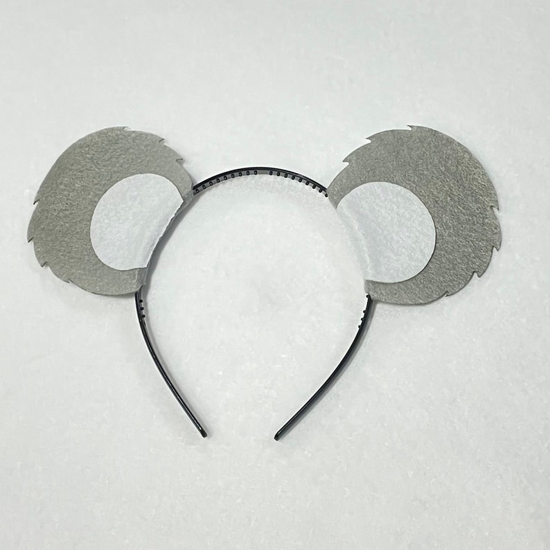 May include: A gray felt koala headband with white felt ears. The headband is black and has a simple design.