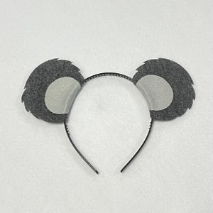 May include: A black headband with two gray felt koala ears. The ears have a white felt circle in the center.