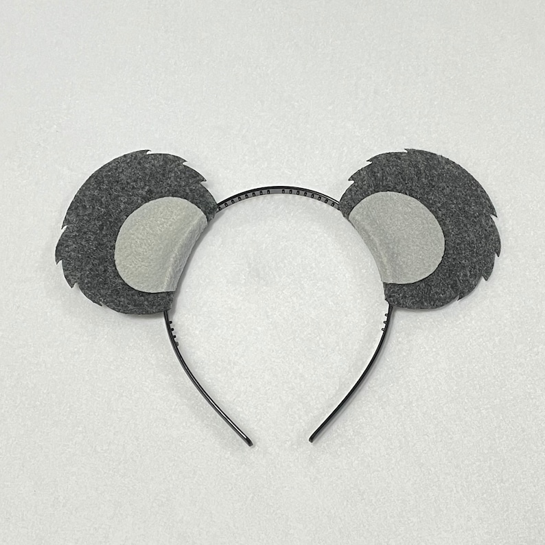 May include: A black headband with two gray felt koala ears. The ears have a white felt circle in the center.