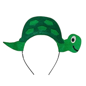May include: Green felt turtle headband with a black headband. The turtle has a shell with a pattern of green squares and a smiling face.