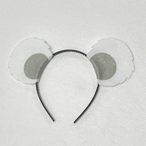 May include: White fuzzy headband with gray felt ears. The headband is black and has a simple design.