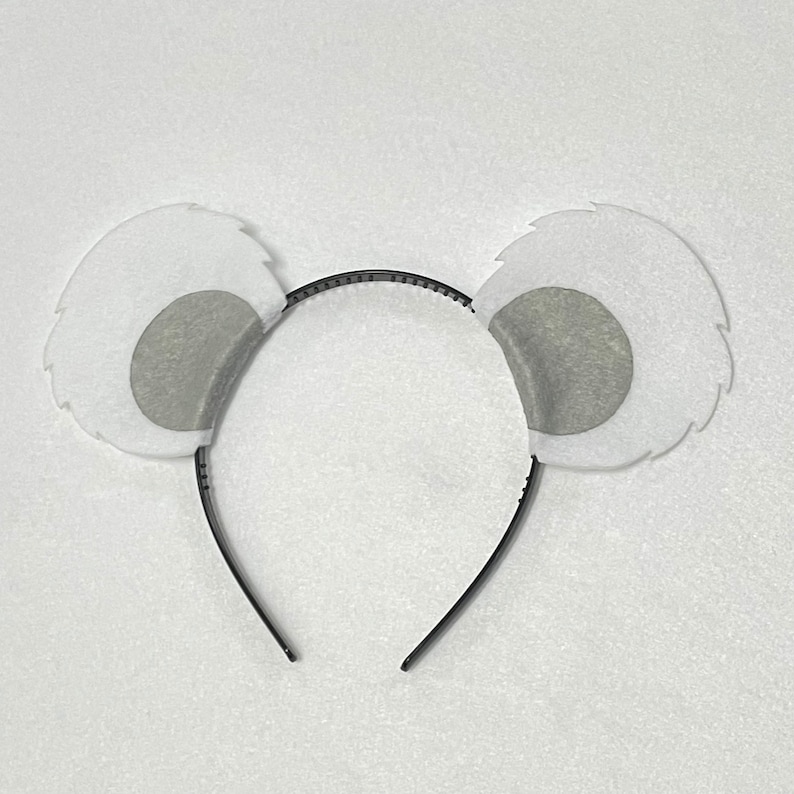 May include: White fuzzy headband with gray felt ears. The headband is black and has a simple design.