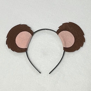 May include: Brown felt bear ears headband with pink felt inside the ears. The headband is black.