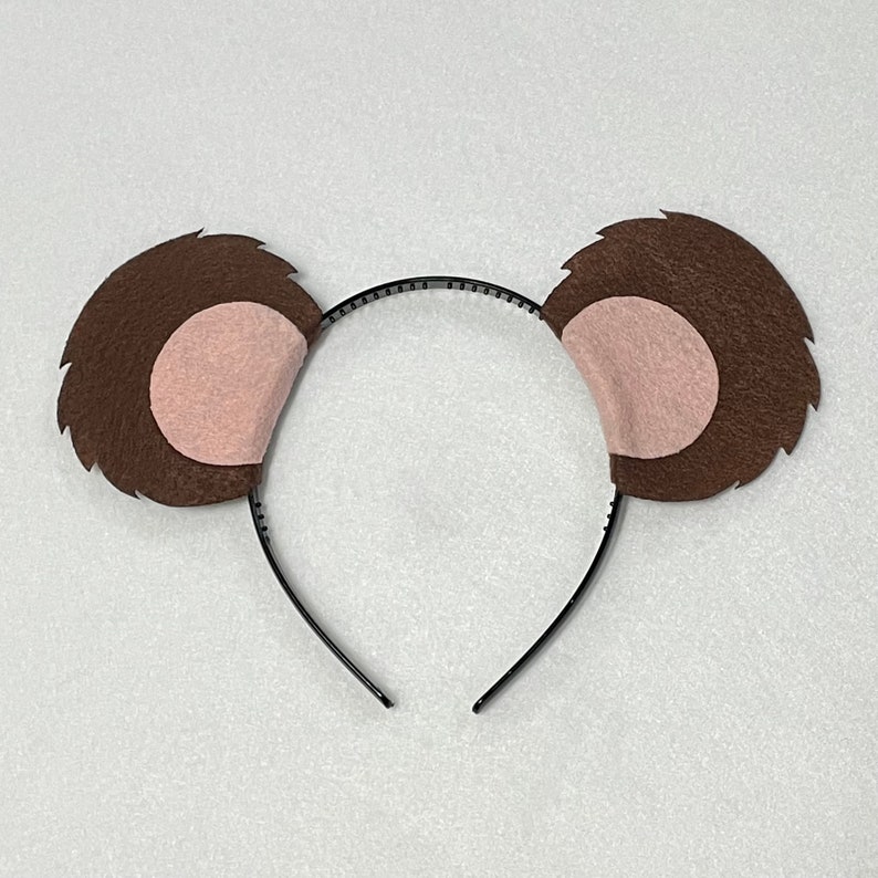May include: Brown felt bear ears headband with pink felt inside the ears. The headband is black.