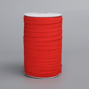 May include: A spool of bright red elastic cord, wound tightly on a white cardboard core.