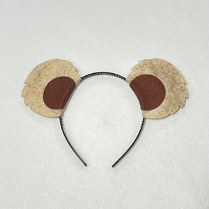 May include: A brown and white felt headband with a black elastic band. The headband is shaped like a pair of ears with brown felt circles in the center.