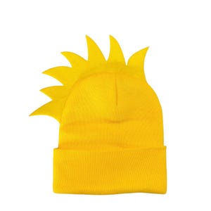 May include: A bright yellow knit beanie featuring a prominent, stiff, sunburst-shaped crest attached to the side. The hat has a wide, folded cuff at the base and a smooth, uniform texture throughout the main body of the headwear.