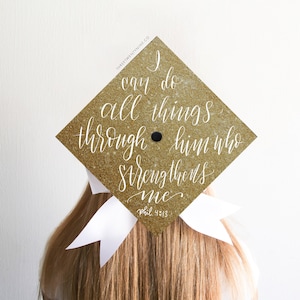 May include: Gold glitter graduation cap with white text that reads "I can do all things through him who strengthens me. Phil 4:13"