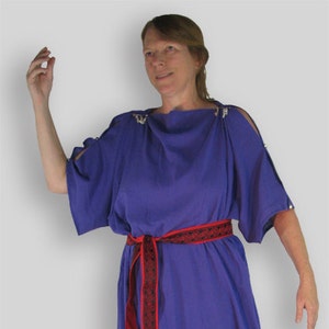 Puede incluir: Un vestido maxi morado con un cinturón estampado en rojo y negro. El vestido tiene un escote redondo y mangas cortas.