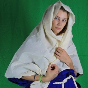 May include: A woman wearing a white linen headscarf with a blue skirt and a white rope belt.
