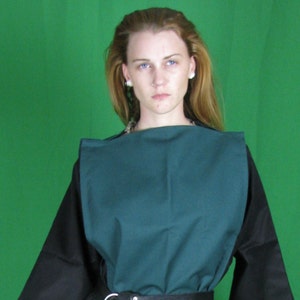 May include: A woman wearing a teal tunic with black sleeves and a brown leather belt. She is wearing brown pants and is barefoot.