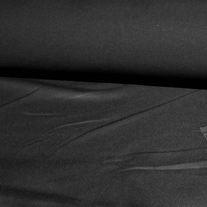 May include: A roll of black fabric, with visible folds and a slightly textured surface. A cut piece of the same fabric lies to the right, showing the raw edge. The fabric appears to be a solid color, suitable for various sewing projects.