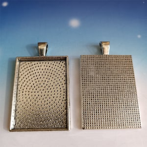 Könnte beinhalten: Zwei silberfarbene Metallbilderrahmen mit einer strukturierten Oberfläche. Die Rahmen sind rechteckig und haben oben eine Schlaufe zum Aufhängen.