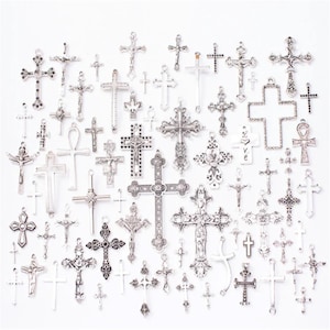 Peut inclure: Une collection de breloques en forme de croix argentées avec différents motifs et styles. Les breloques sont disposées de manière aléatoire sur un fond blanc.