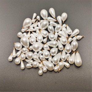 May include: A large pile of white pearl teardrop beads with gold jump rings. The beads are various sizes and shapes.