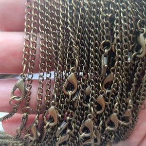 May include: A close-up of a pile of gold-toned metal chains with lobster claw clasps. The chains are all the same length and are arranged in a neat pile.