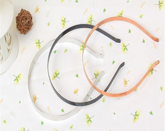 May include: Three metal headbands in silver, black, and brown. The headbands are lying on a white surface with a floral pattern.